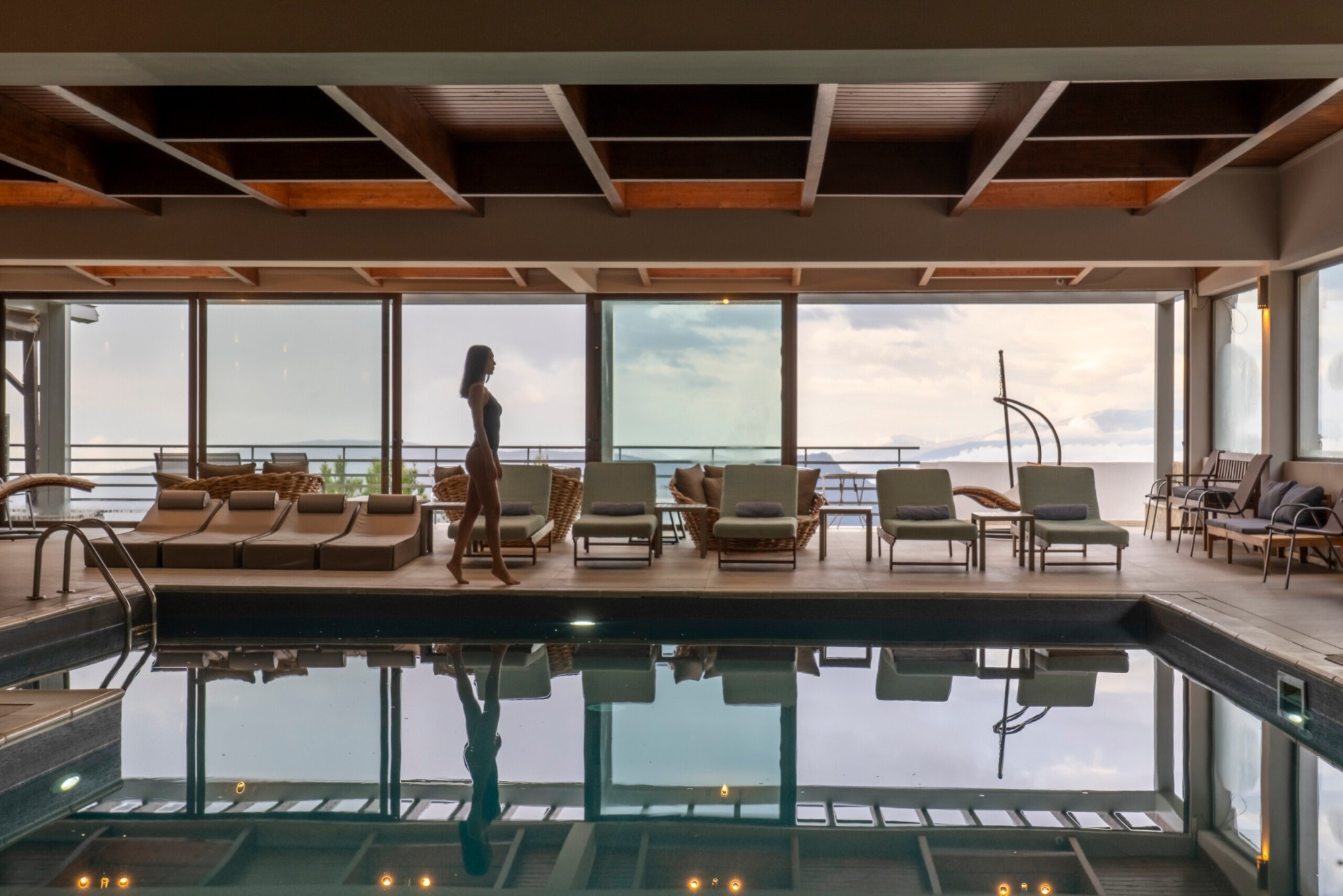 Indoor pool with a wooden beam ceiling and mountain views, a guest walking along the pool deck