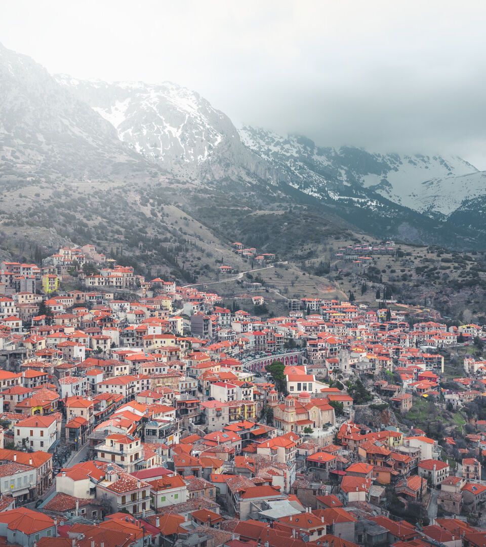 Aerial view of Arachova with red-tiled roofs below snow-capped mountains