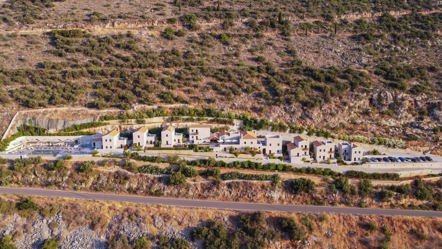 Aerial view of the stone buildings and pool of the hotel on a Mani hillside