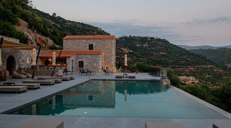 Infinity pool and stone restaurant building at dusk, with hills beyond