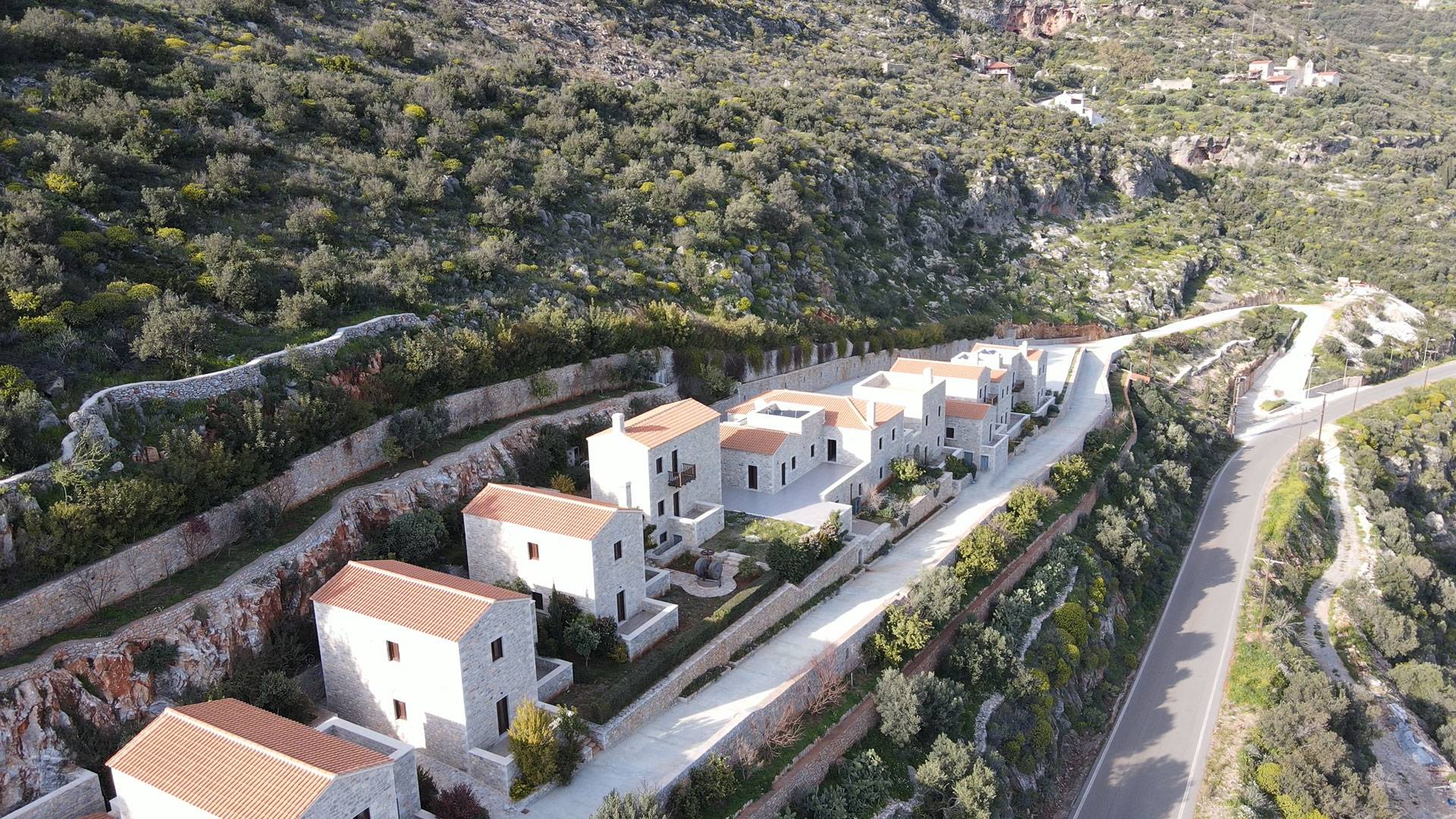 Aerial view of stone villas with terracotta roofs beside a mountain road