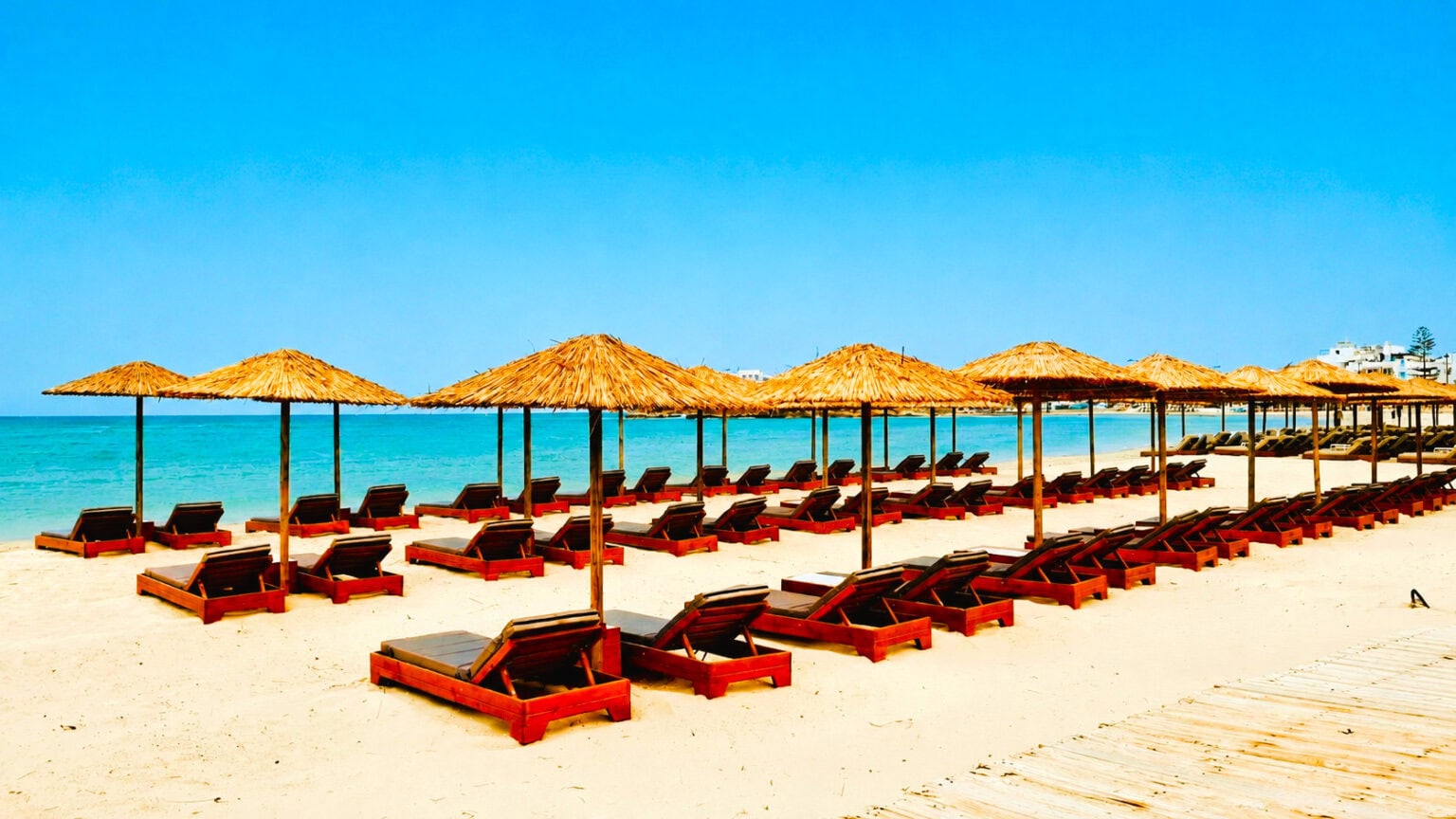 Rows of loungers under thatched umbrellas on a white-sand beach