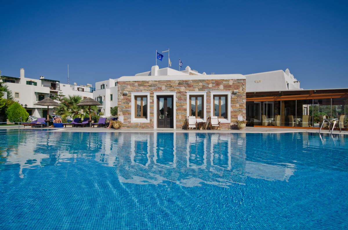 Large blue pool in front of a stone-clad whitewashed building with Greek and EU flags