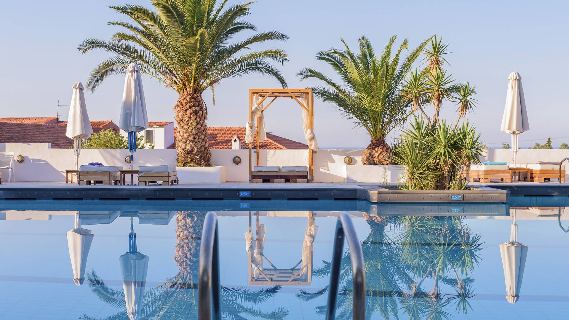 Pool with palm trees, white terrace walls and red-tiled roofs reflected in the water