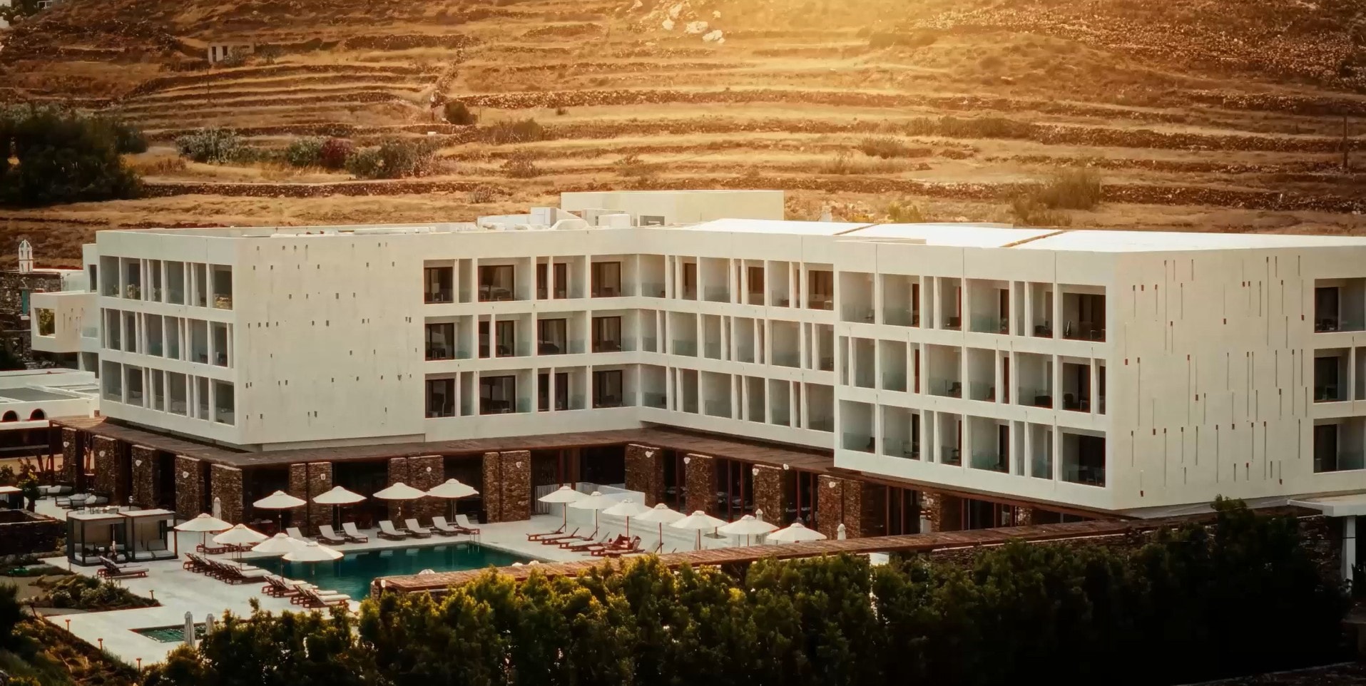 White hotel with a pool at golden hour in front of terraced hills
