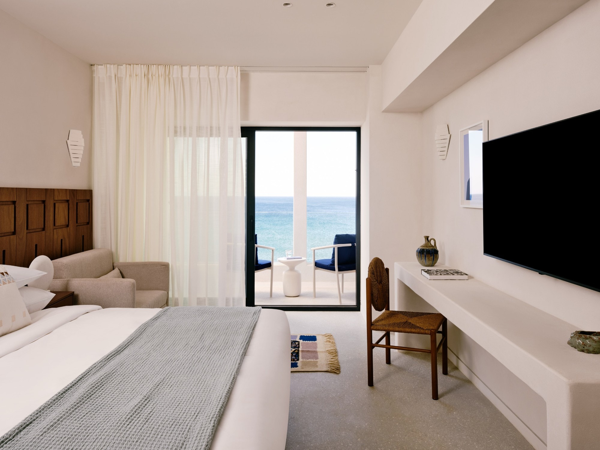 Bright white bedroom opening onto a balcony with a view of the sea